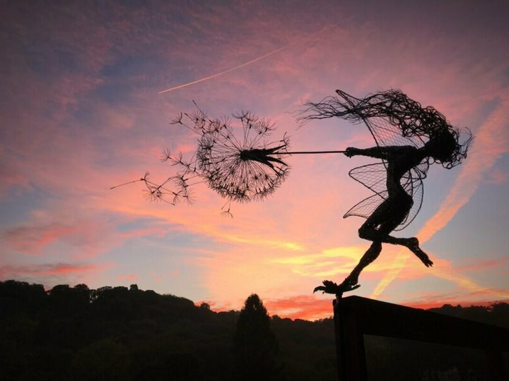 Whimsical metal fairy with lifelike dandelion stakes, ideal for enchanting garden decor, adding magic to outdoor spaces.